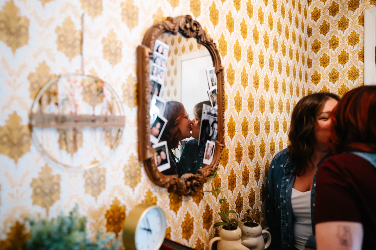 Queer couple kissing in front of a vintage mirror during an intimate at-home engagement session.