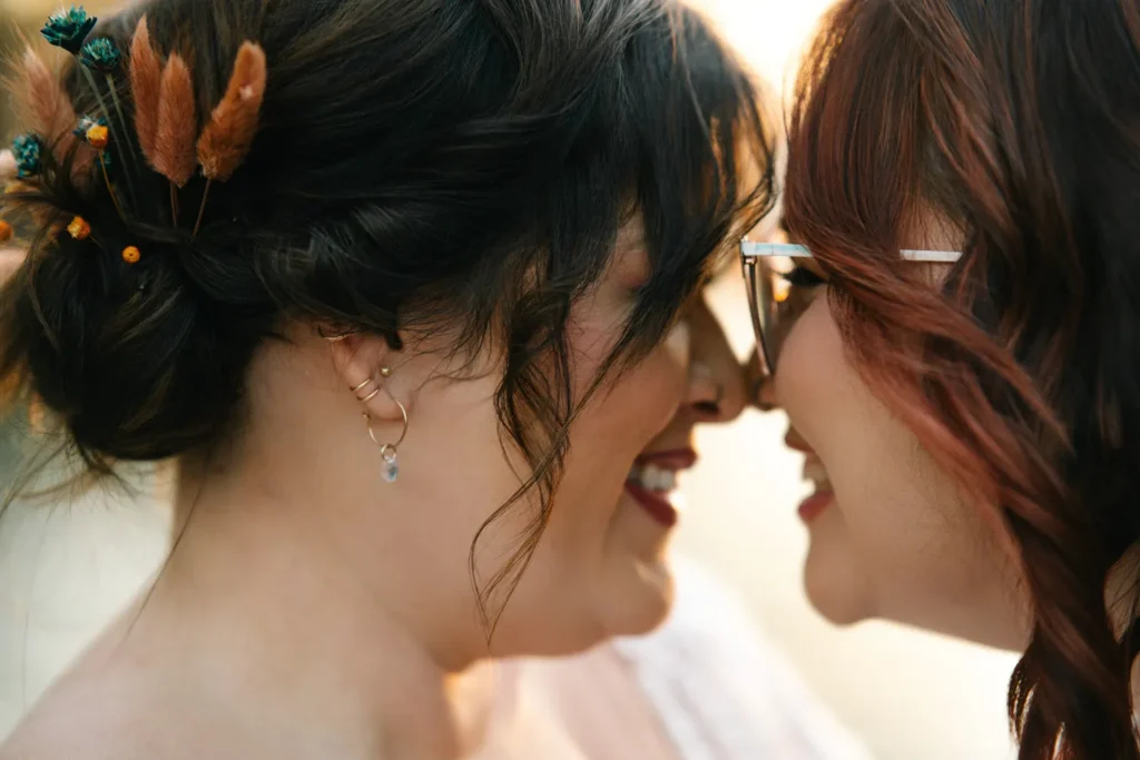 Close-up of two brides laughing with their foreheads touching during an intimate wedding ceremony.