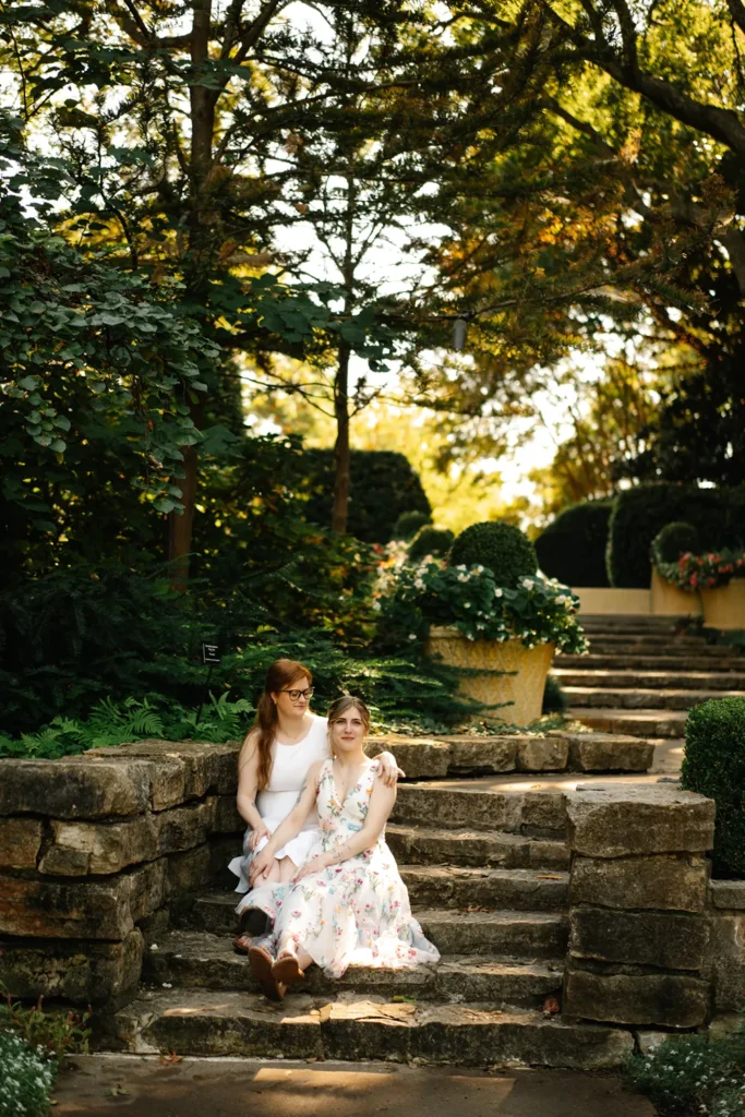 Darcy and Kassidy sitting together on stone steps during their queer elopement at the Dallas Arboretum.