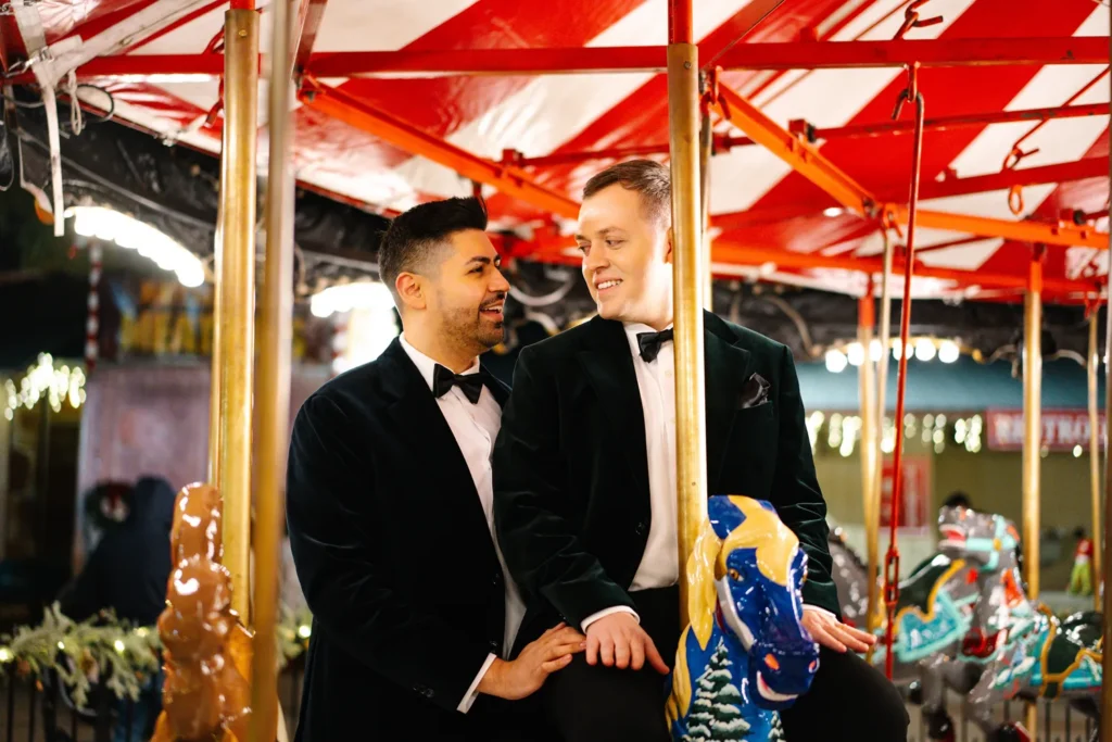 Gay couple smiling at each other while riding a carousel during a Christmas engagement session in Grapevine, Texas.
