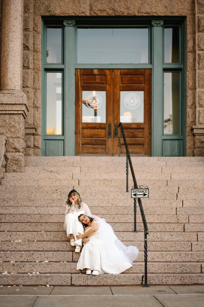 Two brides sit together on the steps outside the Fort Worth courthouse after their queer LGBTQ elopement.
