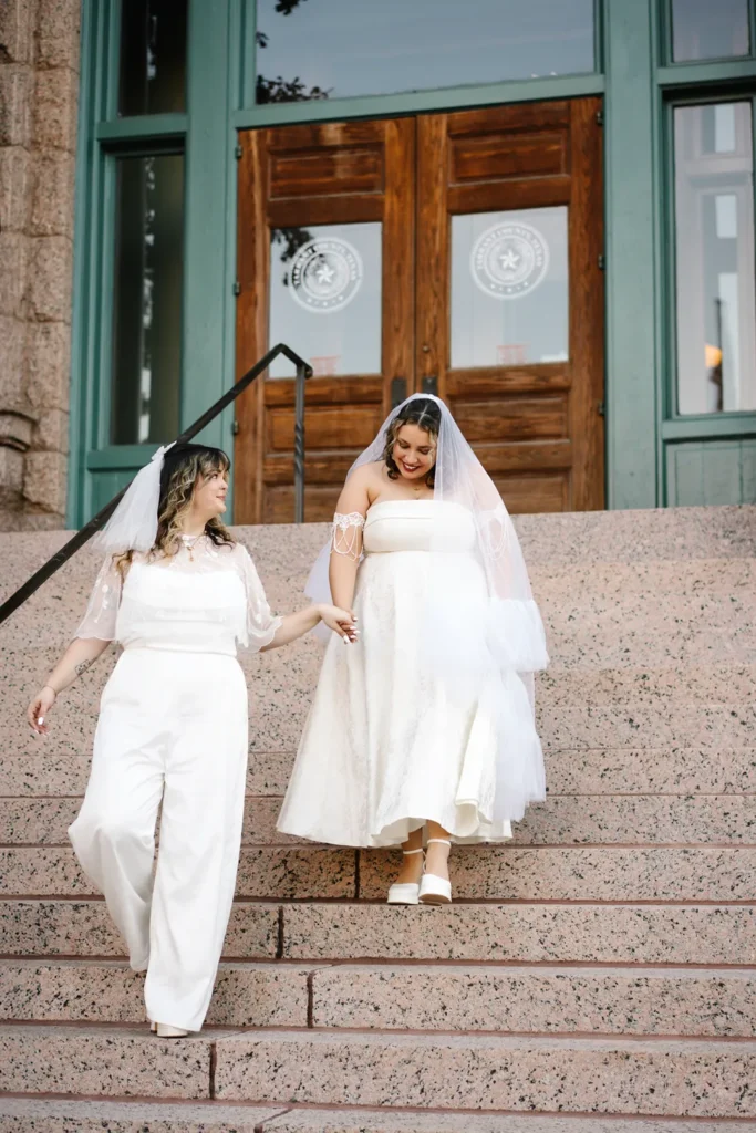 Two brides walk hand in hand down the steps of the Fort Worth courthouse after their queer LGBTQ elopement ceremony.