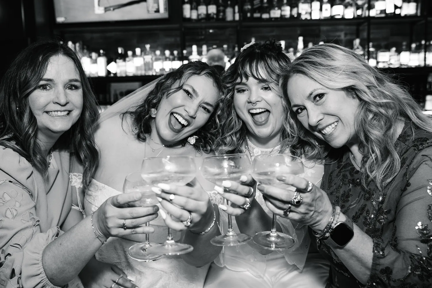 Two brides celebrate their queer LGBTQ Fort Worth courthouse elopement with friends while toasting drinks at a bar.