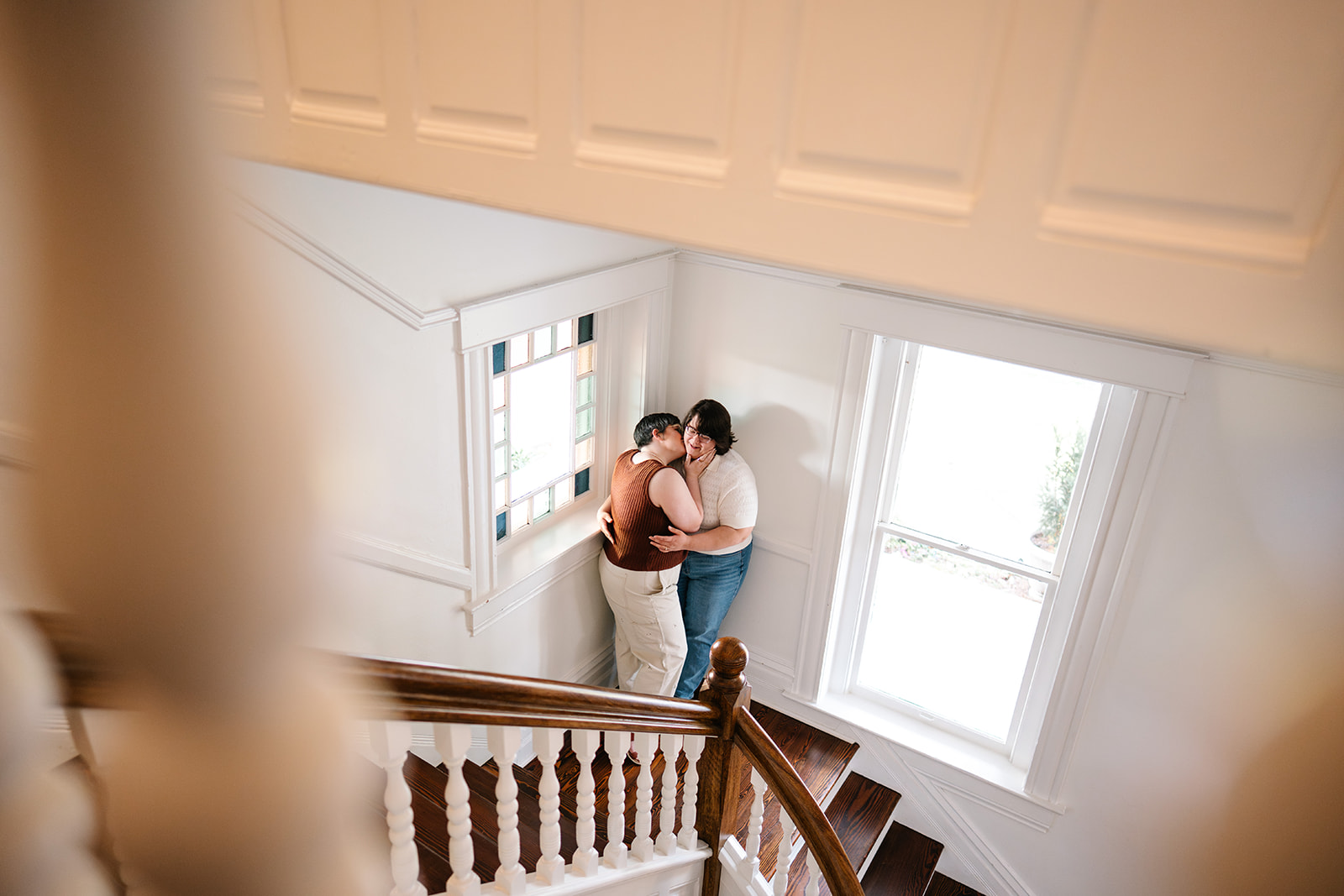 Two women embrace on a historic staircase during an LGBTQ engagement session in Little Rock, Arkansas